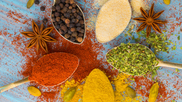 Milled spices - garlic, turmeric, paprika, anise, oregano, cardamom. Round of golden spoons on blue wooden table. Top view, close-up