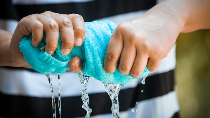Woman hands squeeze wet blue towel and water drop